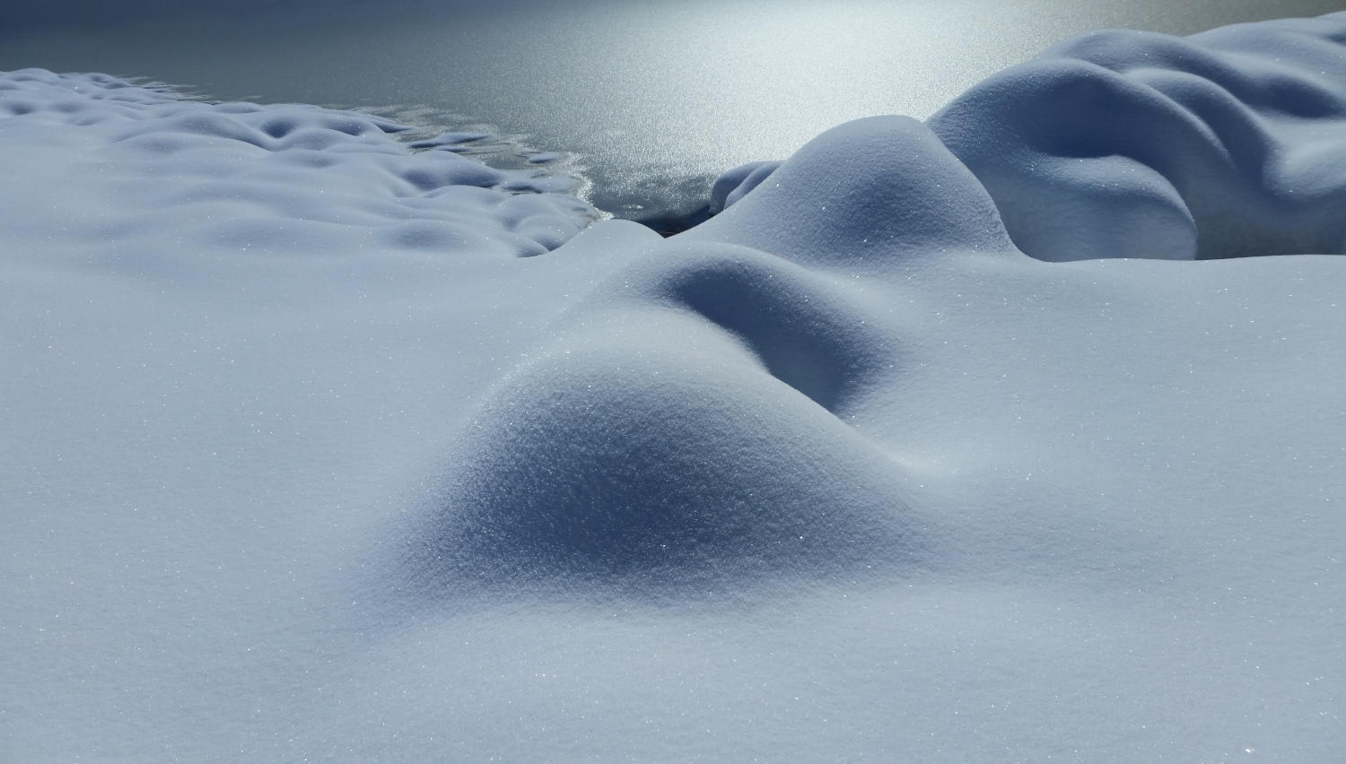 Beautiful blue patterns in snow with a small lake beyond. 